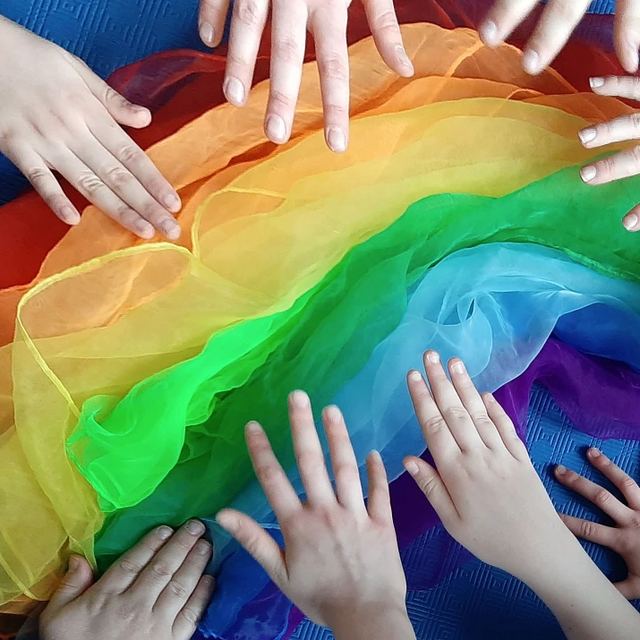 Kinderhände auf einem Regenbogen aus bunten Tüchern