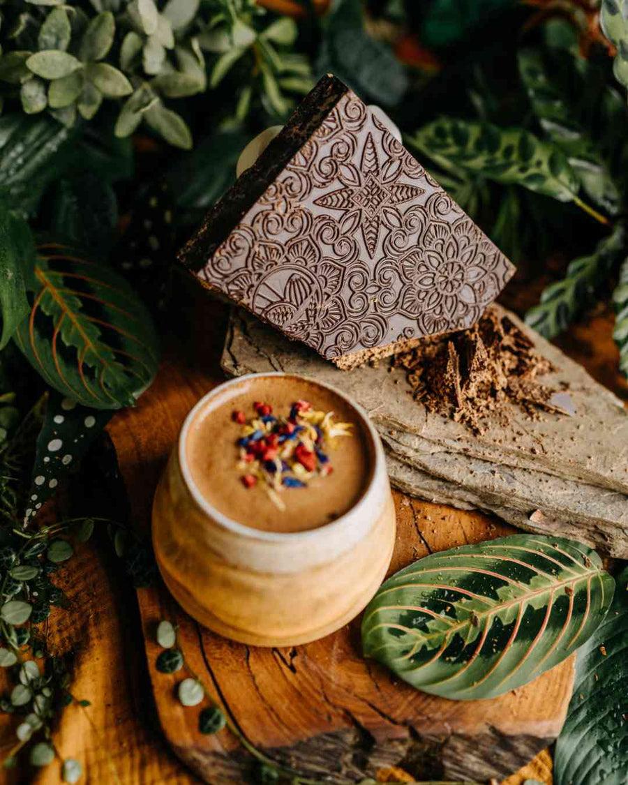 Kakaotafel mit Mandala-Prägung und eine Tasse Kakao zwischen Pflanzen