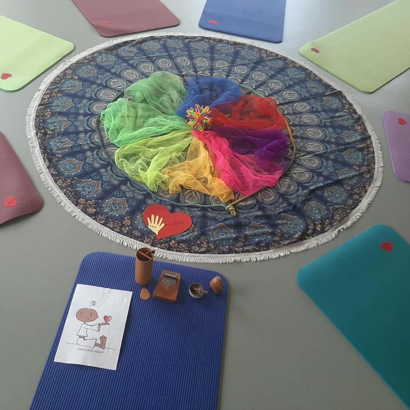 Yogamatten im Kreis um eine Mandala-Decke mit bunten Tüchern und Klanginstrumenten