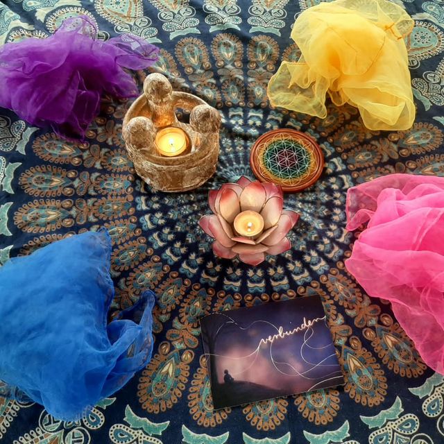 Bunte Tücher, Kerzen und eine Lotusblüte im Kreis auf einer Mandala-Decke